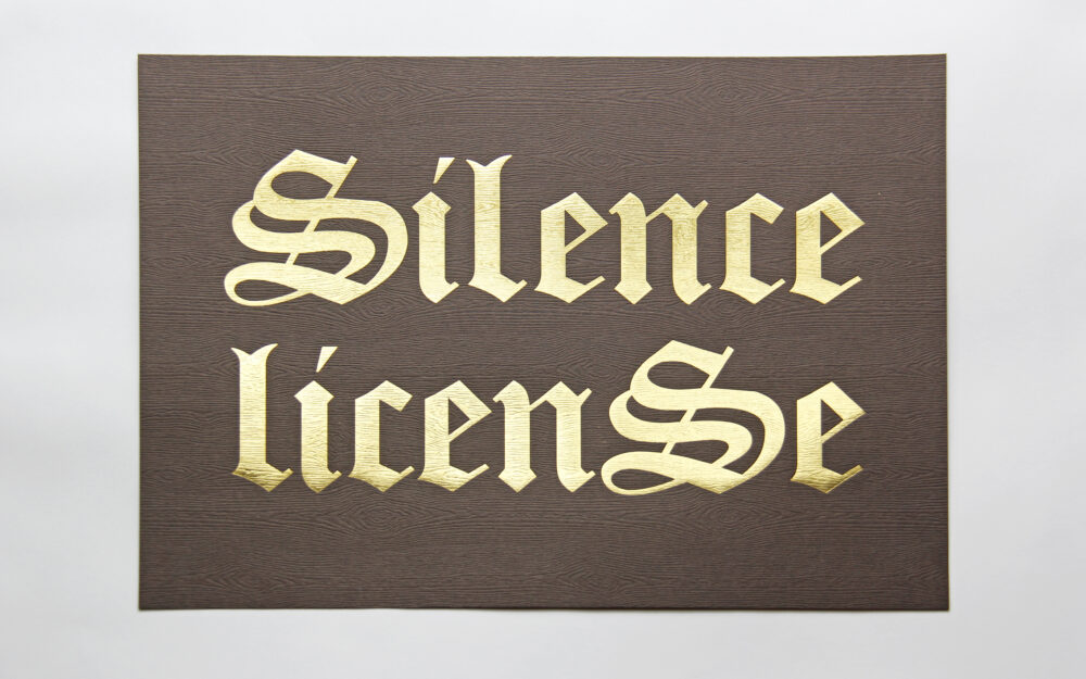 A print with "Silence License" written in gold lettering on brown wood grain paper background.