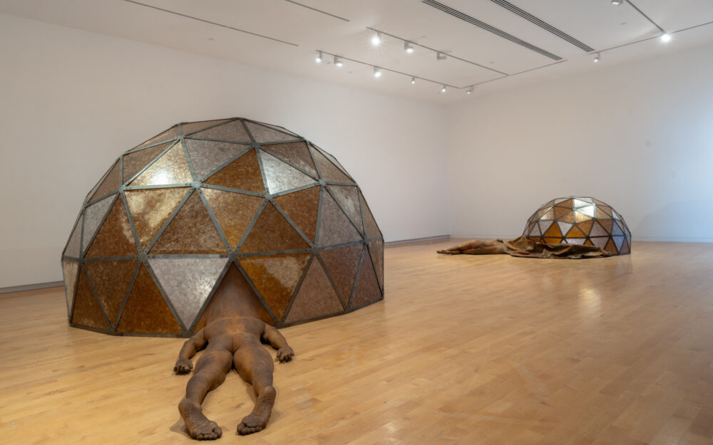 Two large-scale sculptures in a gallery with figures attached to geodesic domes.