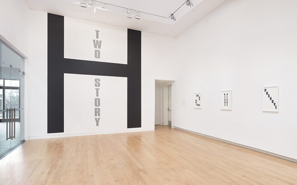 Large black H on gallery wall with the words "Two Story," in gray