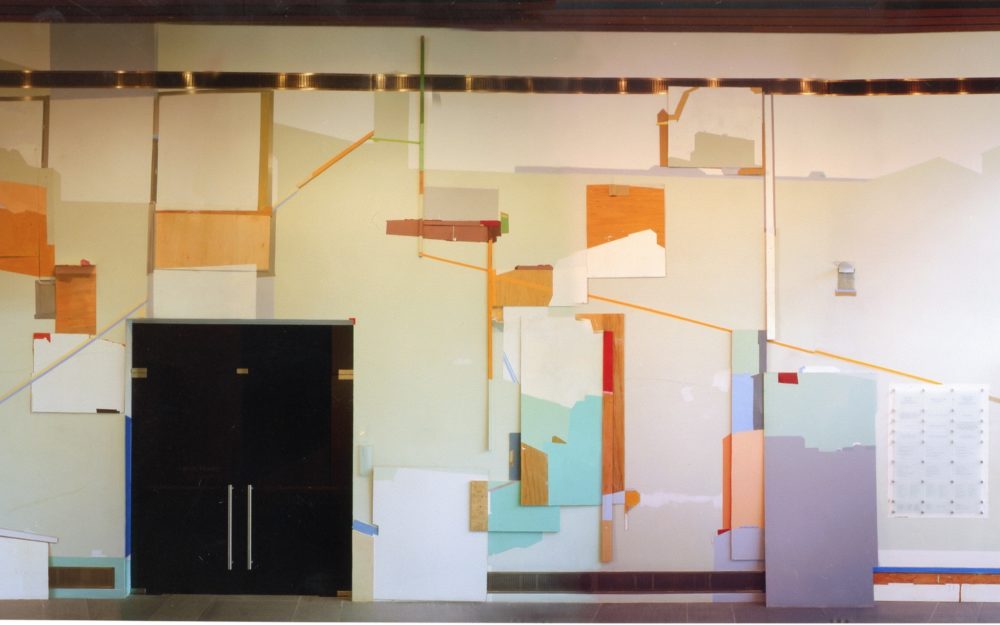 In Atrium Gallery: Colorful, abstract shapes on white wall; L-R; wooden building support, black metal doors, plexiglass box.