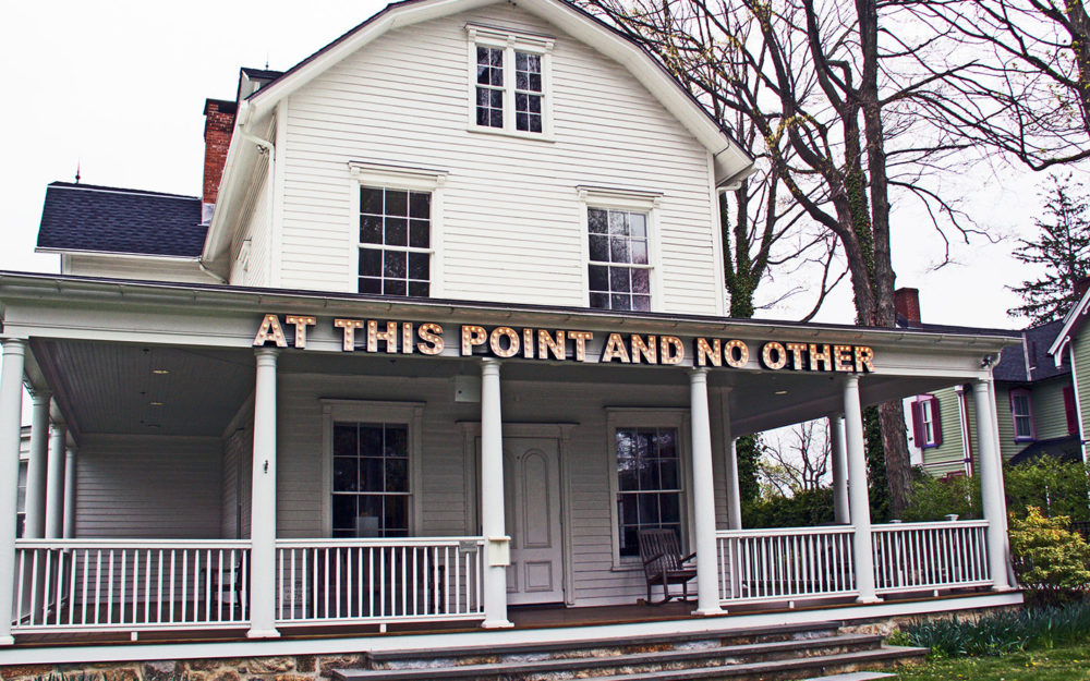 White building with letters reading "At This Point and No Other," on front porch