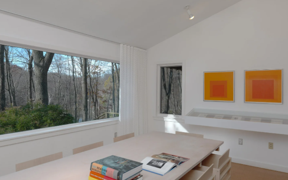 Interior view of the Albers Foundation with a table with books on it and two square orange paintings to the right and a big window looking at nature to the left