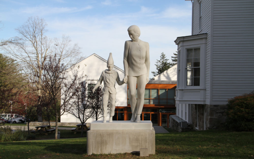 Small sculptural figures walk hand and hand with Museum in the background