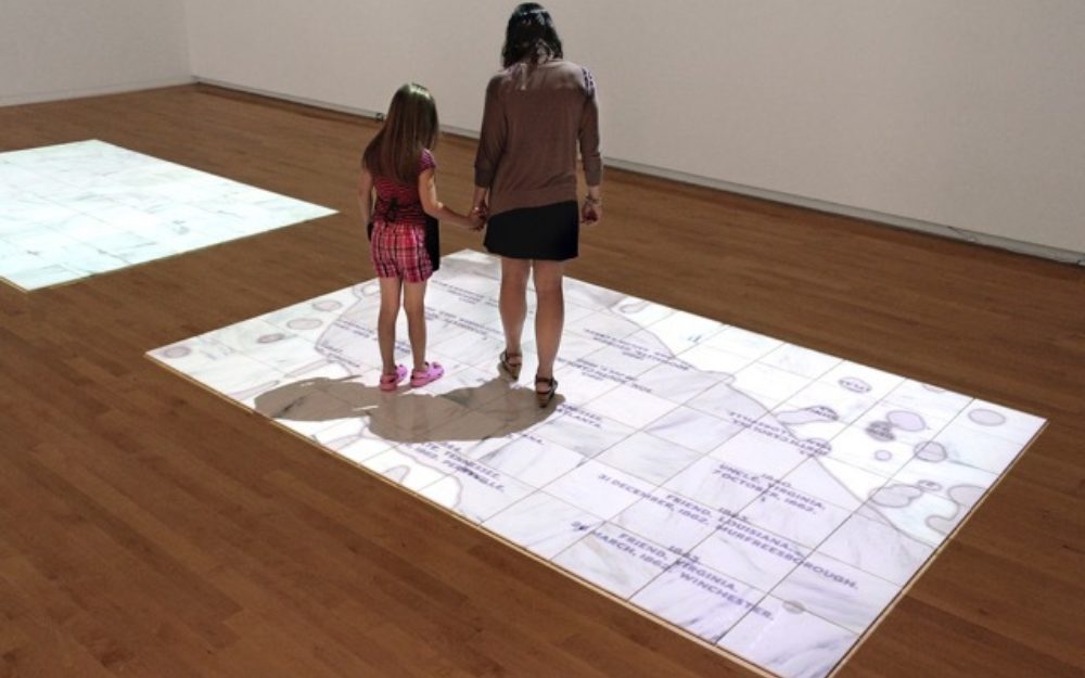 Two visitors look down at a work of art projected on the gallery floor