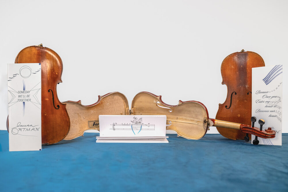 Three boxes made of violins with musical score booklets positioned on blue velvet.
