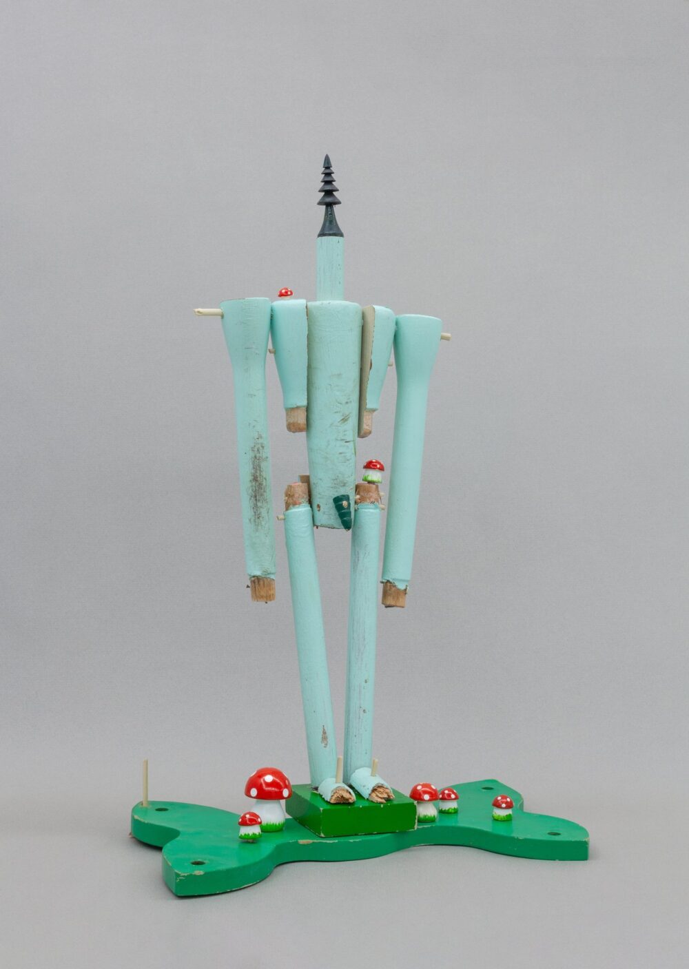 A small light blue wooden figurative sculpture with wooden mushrooms at its feet.