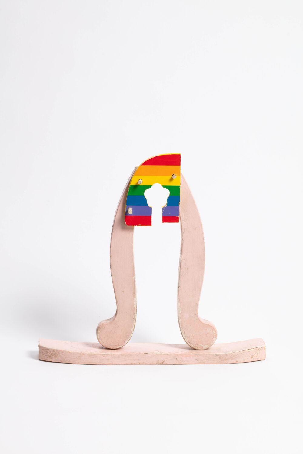 A small wooden sculpture with a pink base and rainbow top with a floral like motif cut away.