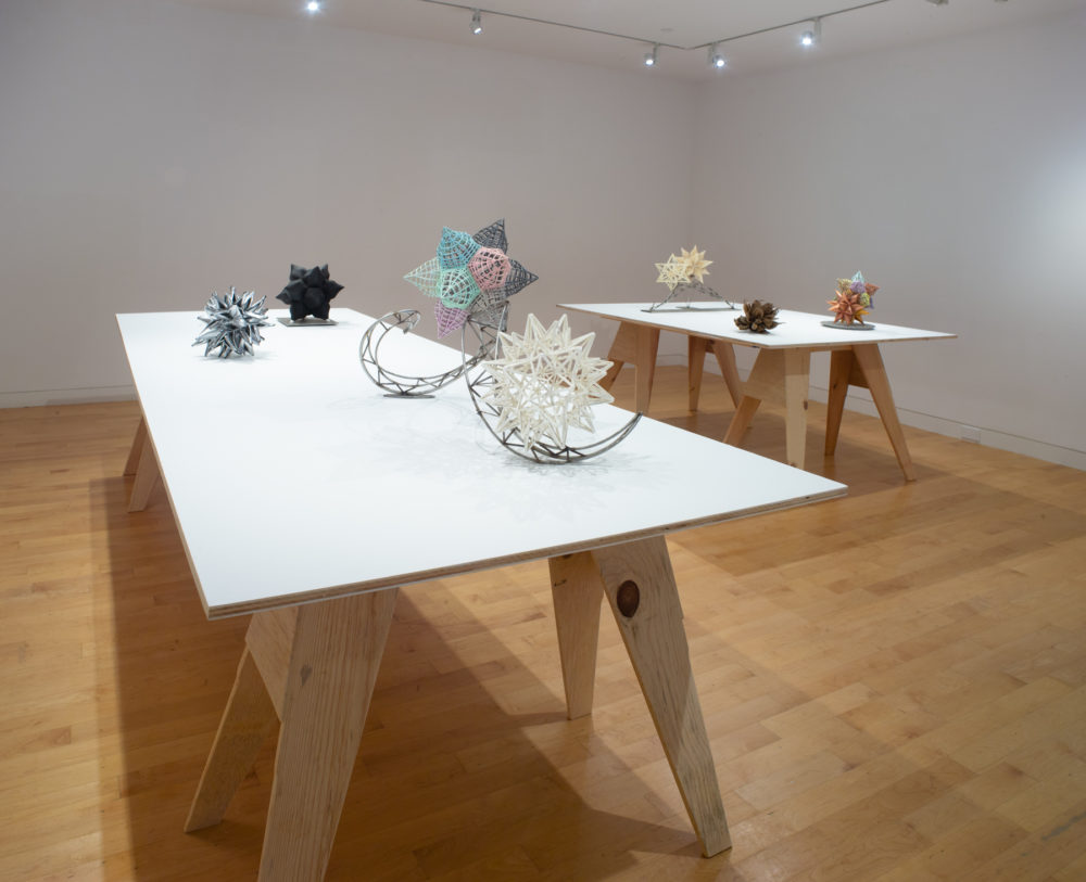Small scale maquettes for larger sculptures by Frank Stella on tables with white surfaces.