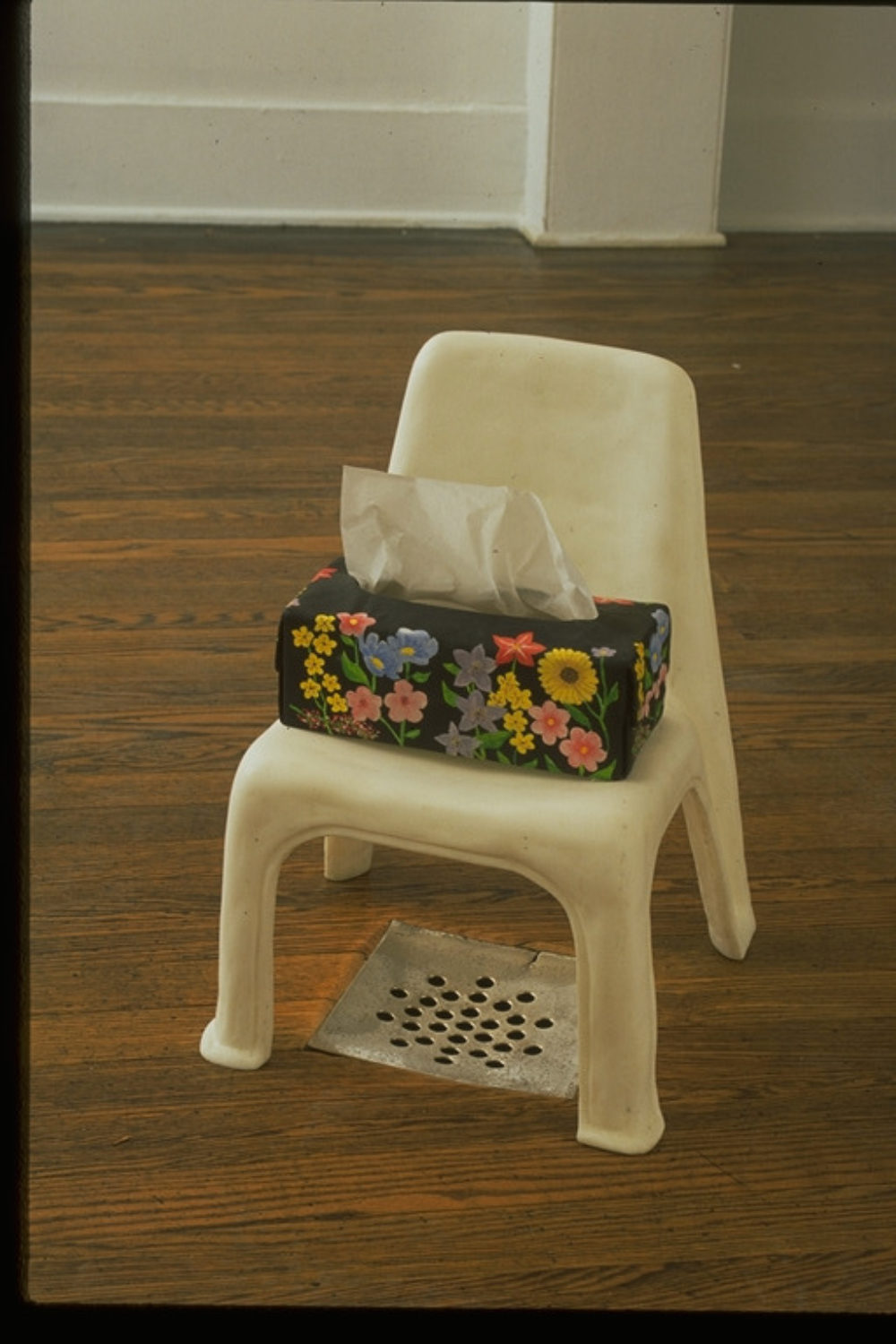 A plastic-appearing chair with a handmade tissue box over a drain in the floor