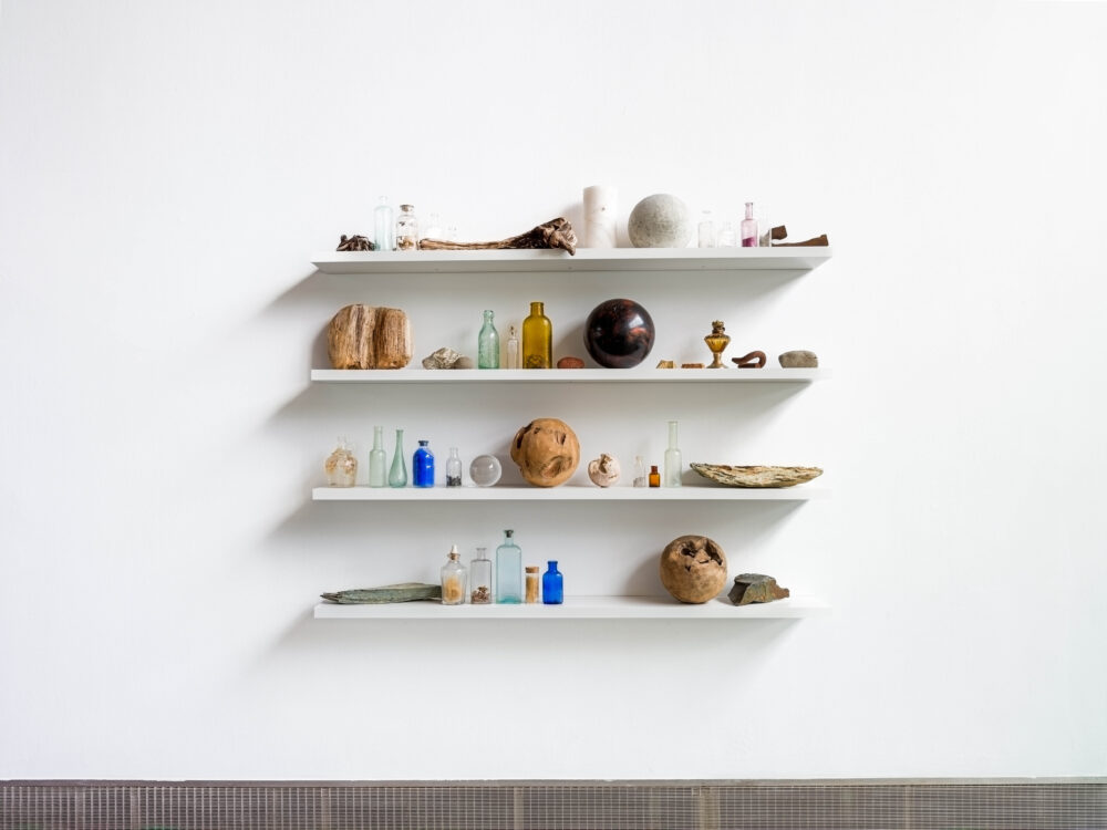 an arrangement of ceramics, stones, and wood pieces displayed on 4 shelves