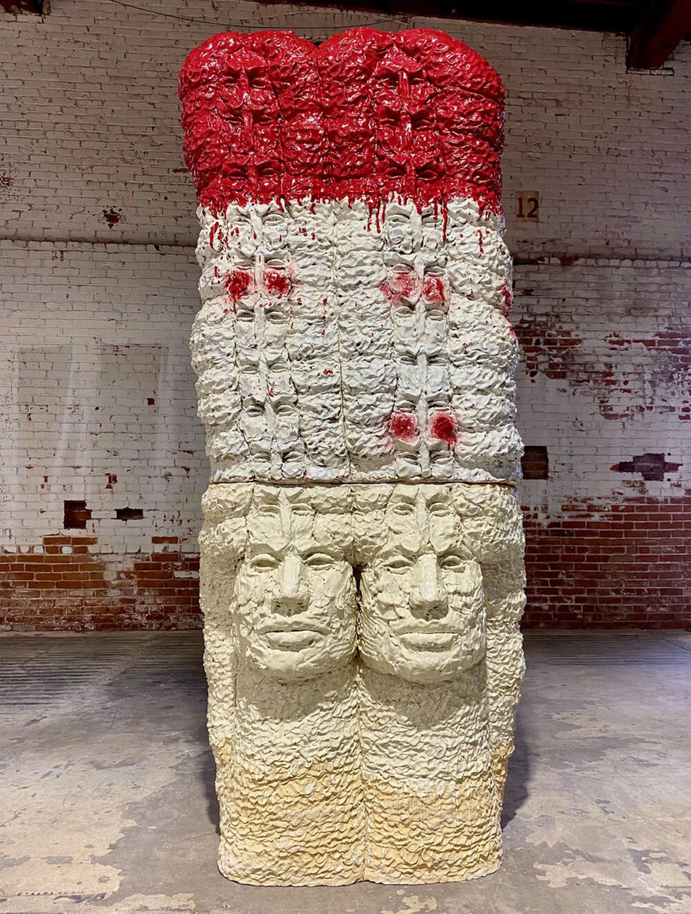 Red, white, and cream colored ceramic sculpture with several faces.