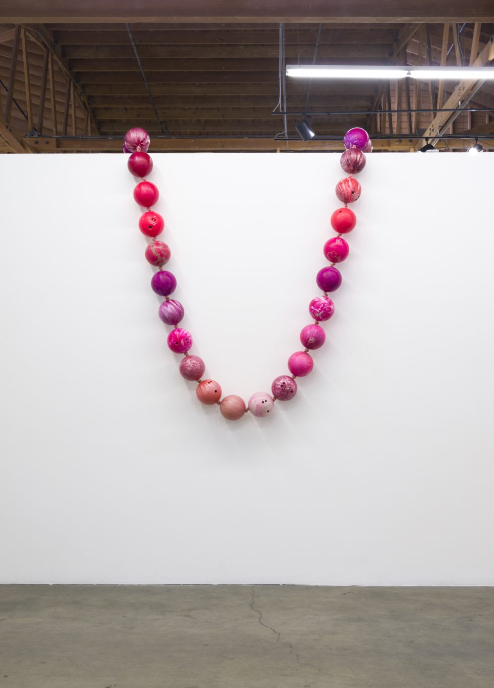 Pink and red bowling balls on a rope hung over a white wall like a string of pearls.