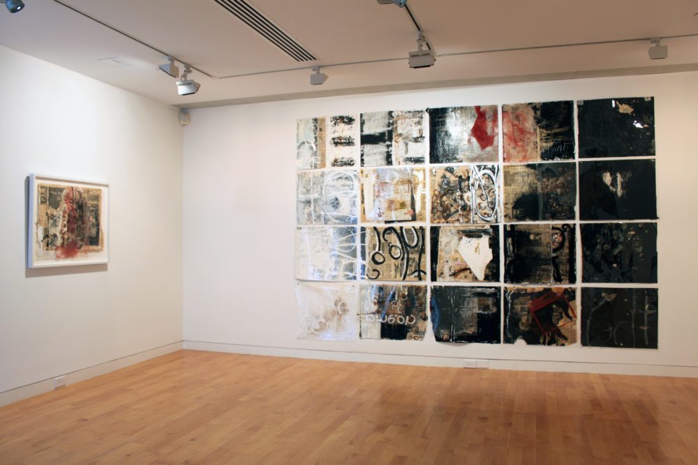 Image of gallery wall with a grid of paintings to the right and a single work to the left.