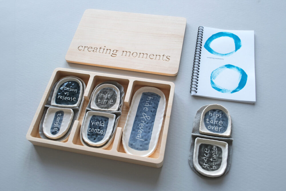 A wooden box with ceramic trays inside with movement prompts and a booklet.