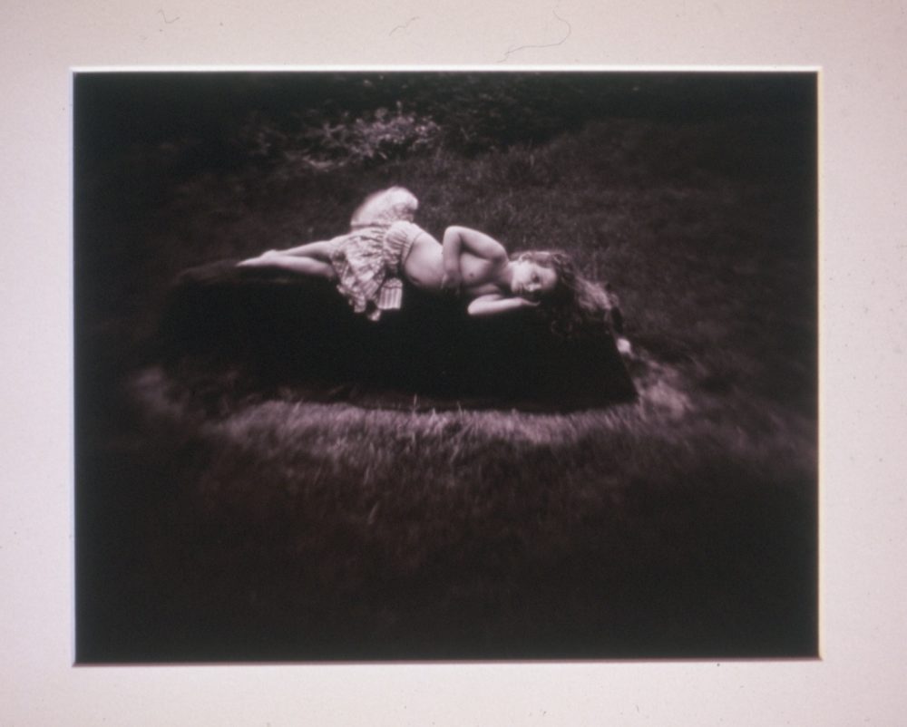 a black and white photograph of a young girl laying sadly on the ground