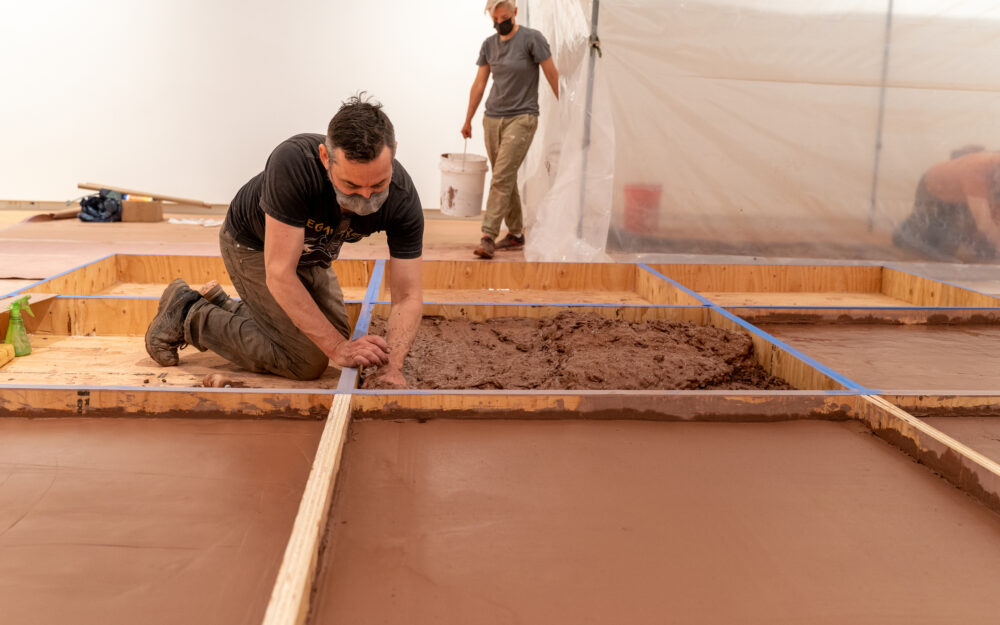 Person pressing wet red clay into a wooden gridded armature.