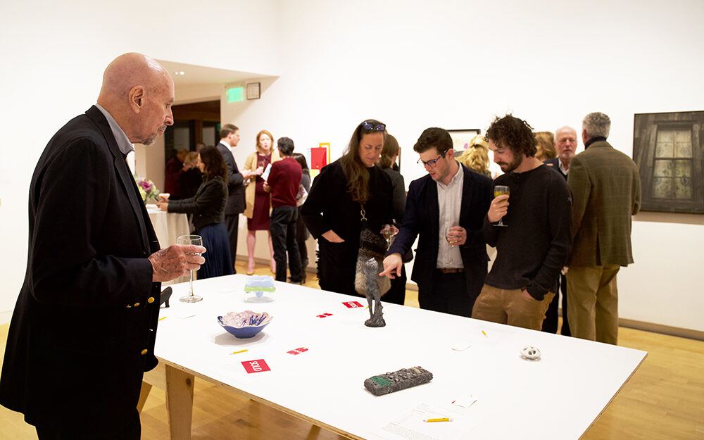 A group of visitors gather around a table with works of art on it