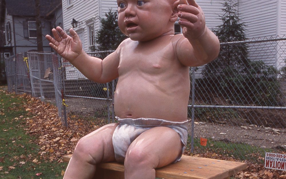 Installation View- Sculpture of giant baby in white diaper. Museum in background.