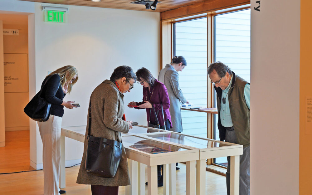 visitors at a museum viewing reading materials displayed on glass a table