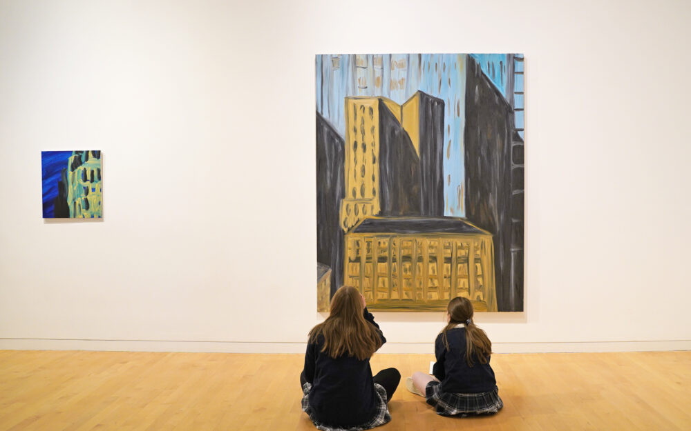 two students sitting on the floor and looking at a painting at an art gallery