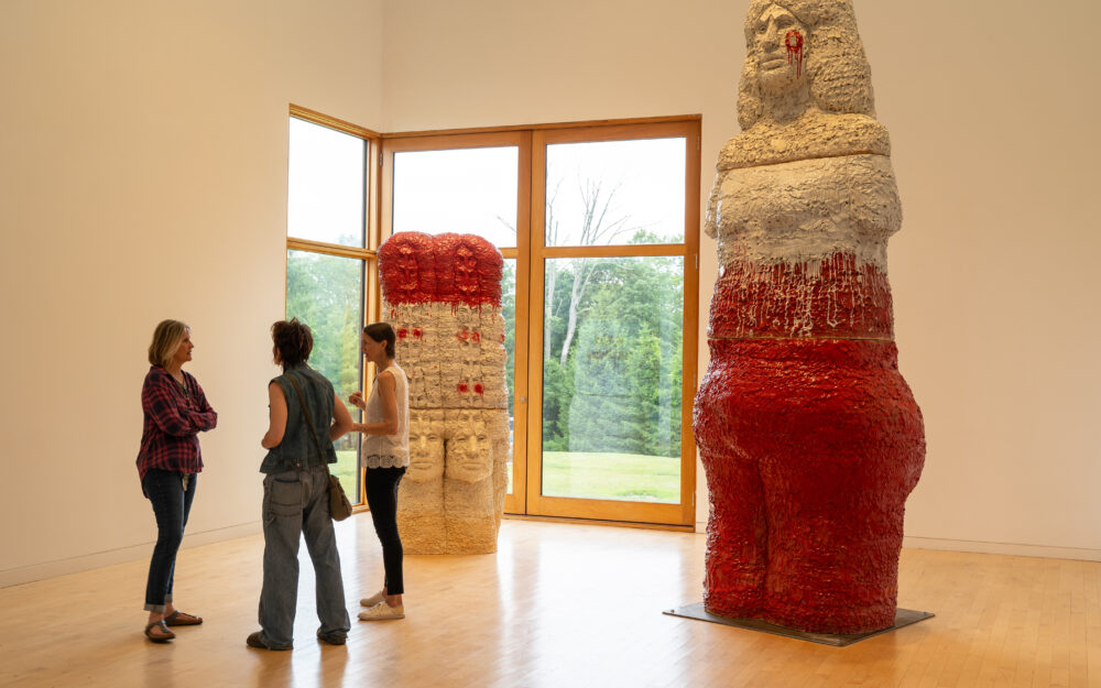 Three people standing in a gallery near large scale figurative sculpture.
