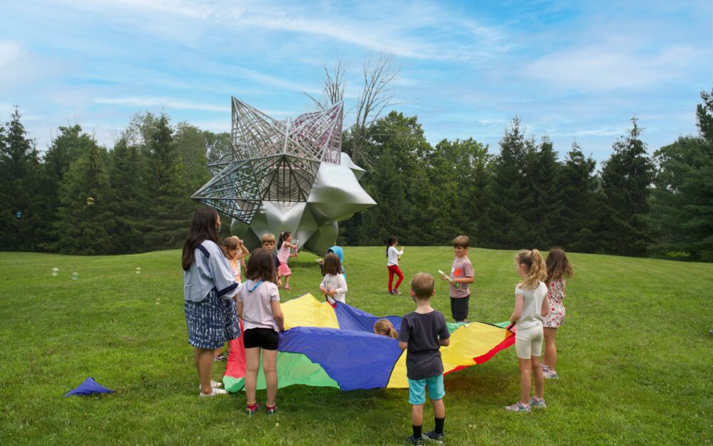 Children and teacher playing outside with a colorful parachute