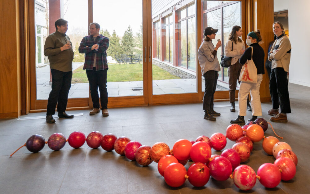 People chatting around a sculpture of a giant pearl necklace made of pink bowling balls boiled on the ground