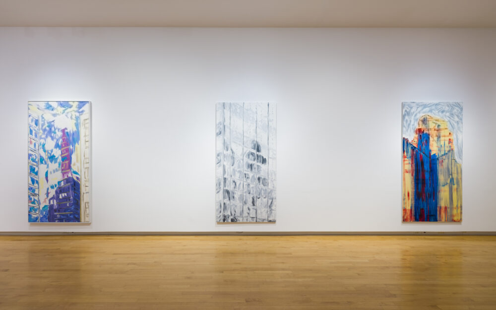 Three large vertical paintings hung on a white wall