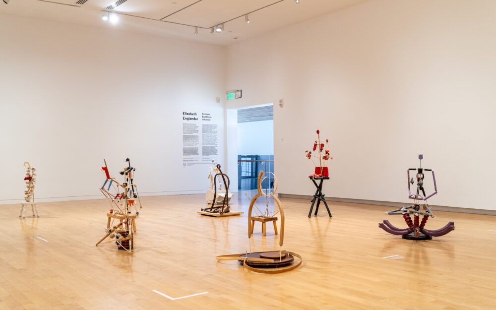 Seated figurative sculptures positioned on a floor in a gallery.