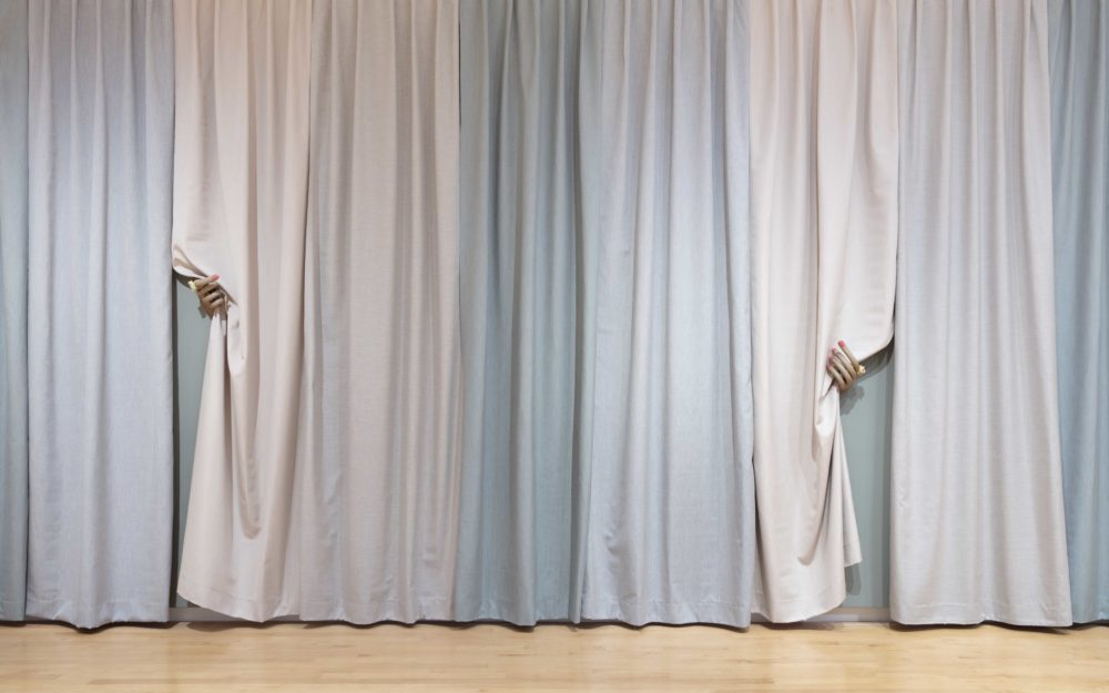 Pastel multi-colored curtain panels with two manicured hands pulling back two pieces of fabric.