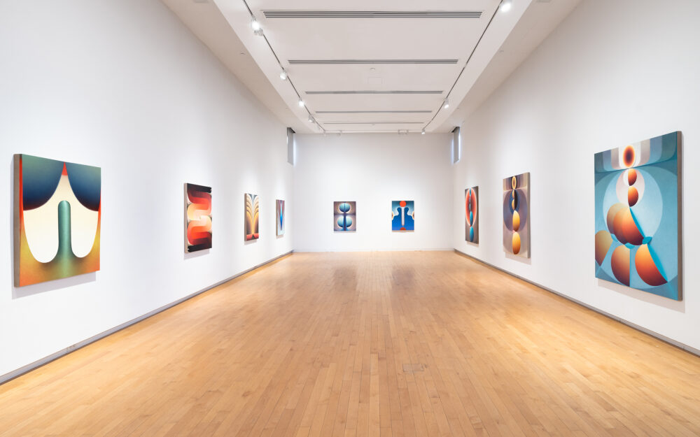 Colorful paintings installed in a row on three walls of a gallery
