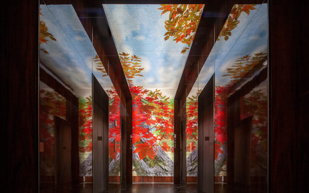 Image of a lobby with elevators with a tapestry of a red maple tree.