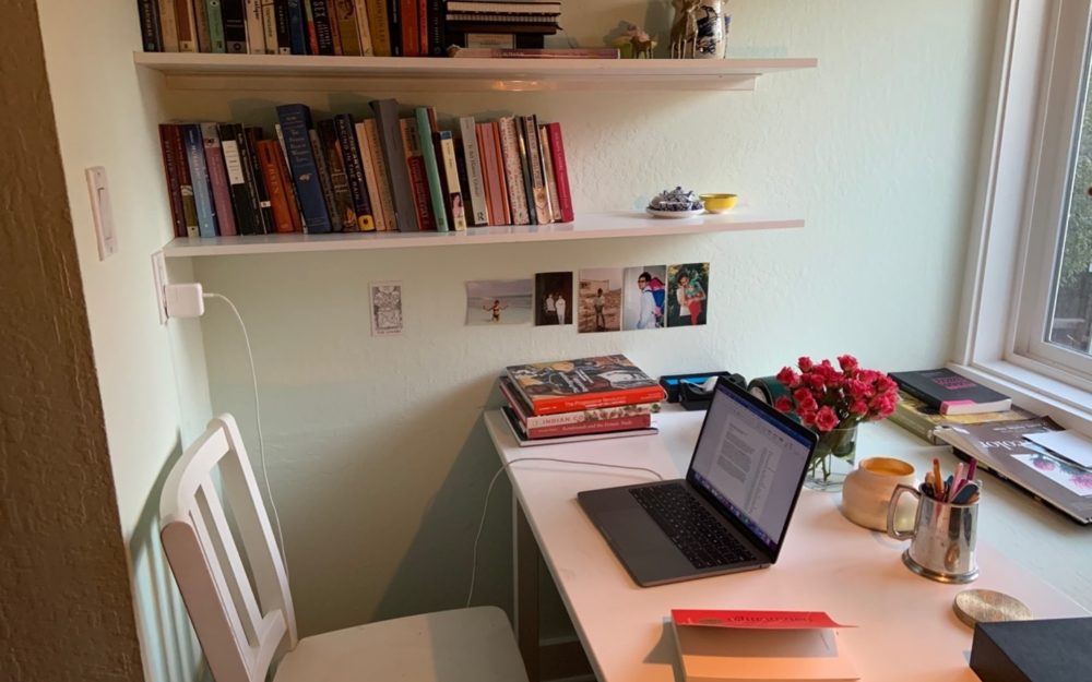Laptop sits open on a desk with a bookshelf in the background