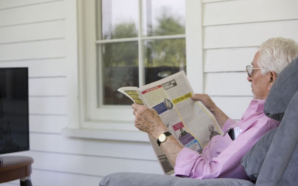 Individual sits in a recliner and reads the newspaper