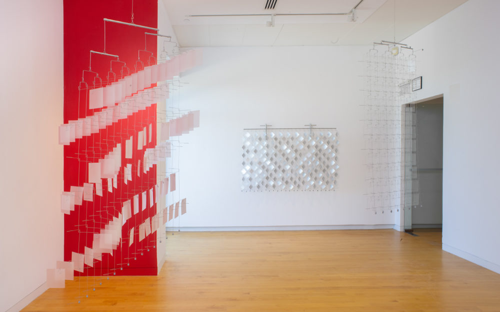 Gallery with one wall painted red and three suspended reflective material and wire sculptures.