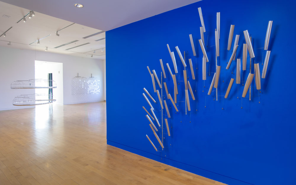 Blue wall in foreground with a silver material and wire sculpture. Two other suspended sculptures in background.