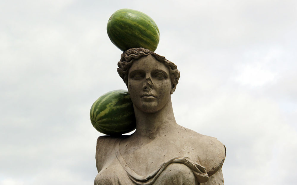 Stone sculpture with two watermelons resting on head