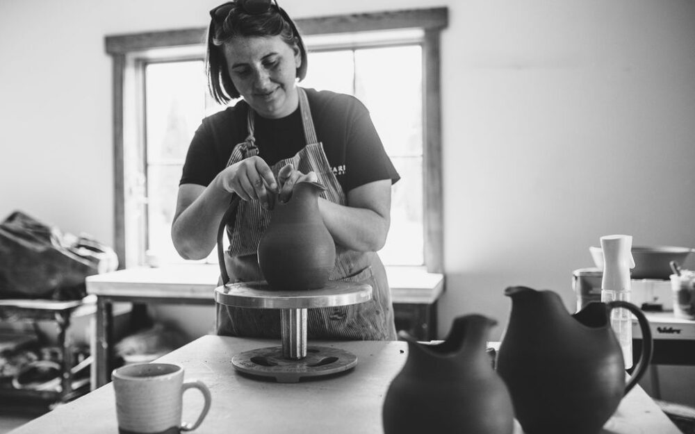 A woman putting a handle on a ceramic pitcher in a studio.