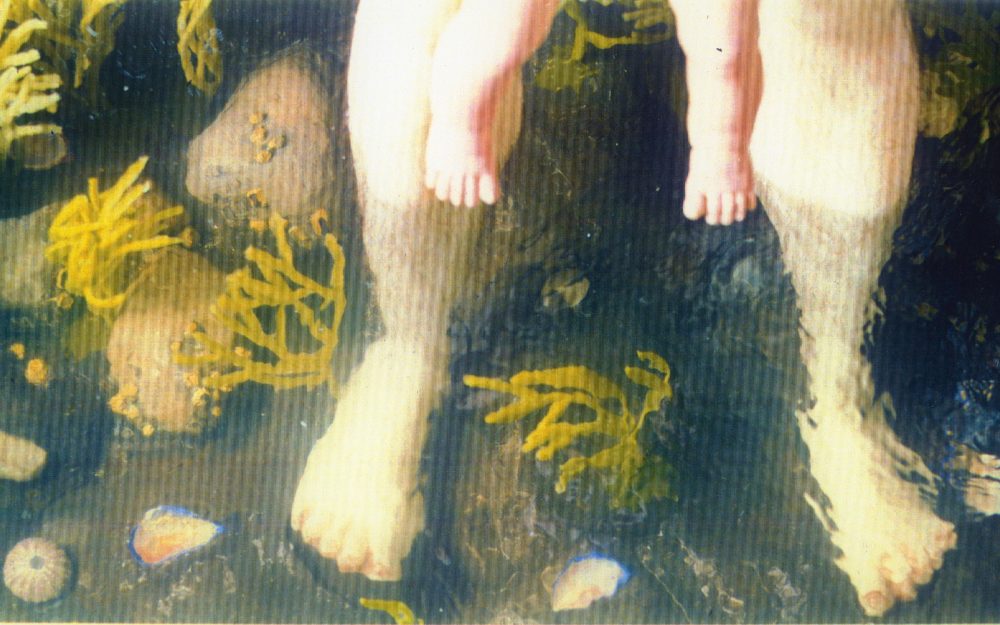 Two pairs of wax legs standing in a false river/ ocean with algae, rocks and water