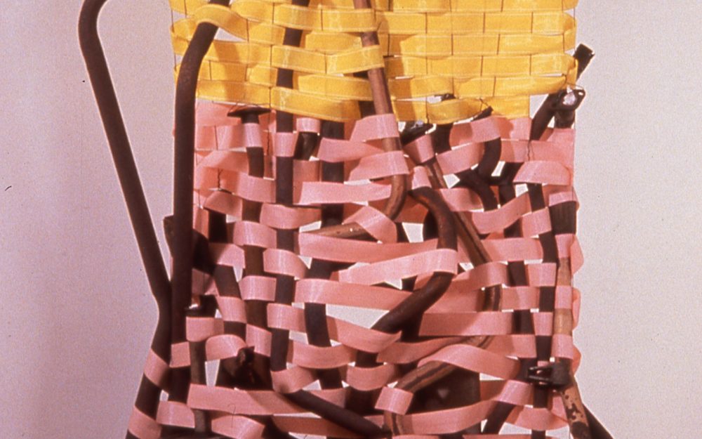 verticle Brown metal vertical structure with thick yellow and pink plastic strips woven in.