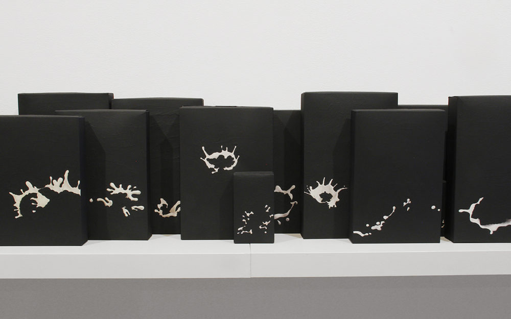 Small black sculptural works on a white shelf