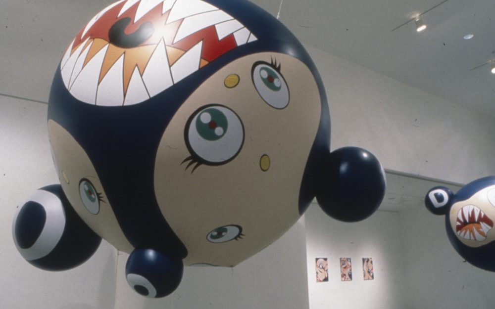 This is a photograph of an installation in the Pop Surrealism exhibition which is blow up work with a large mouth bearing sharp teeth and sweet cartoonlike eyes