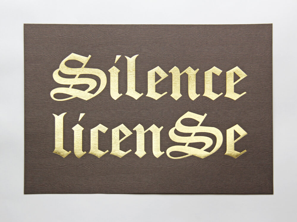 A print with "Silence License" written in gold lettering on brown wood grain paper background.