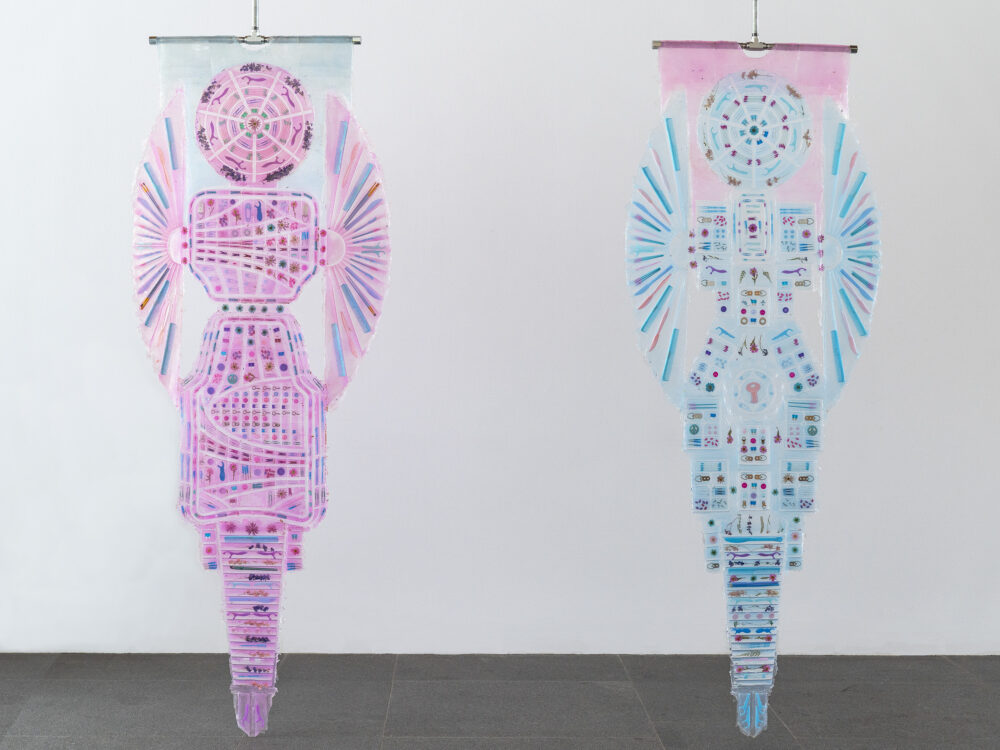 Two hanging transparent sculptures with small objects embedded within.