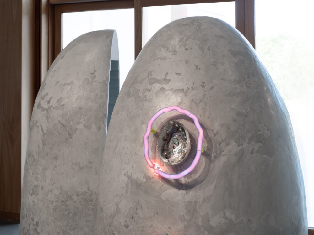 Detail of large sculpture focused in on a circular neon element around a shell.