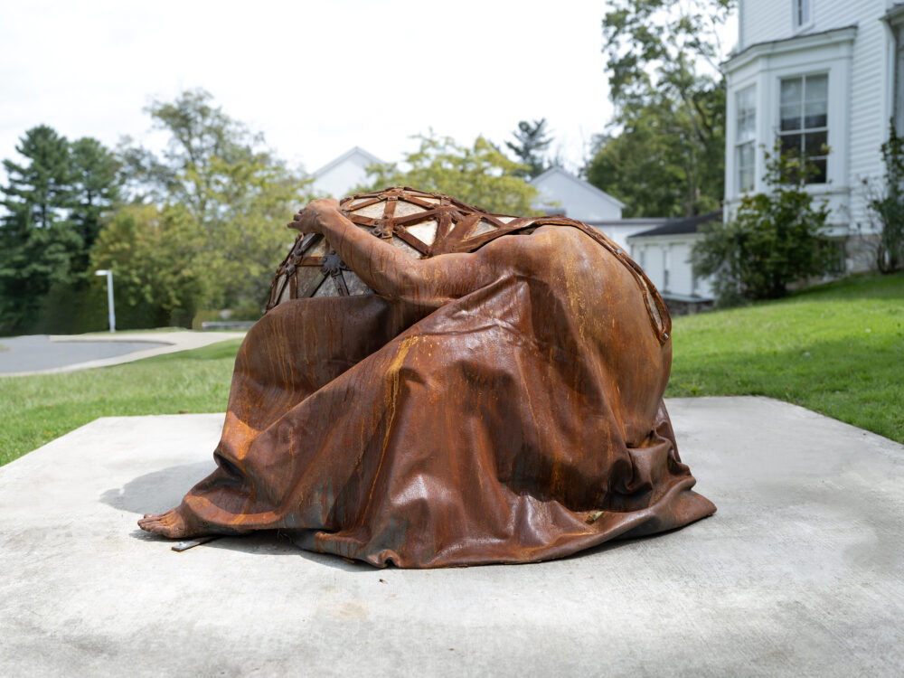 An outdoor sculpture with a figure embracing a geodesic dome.