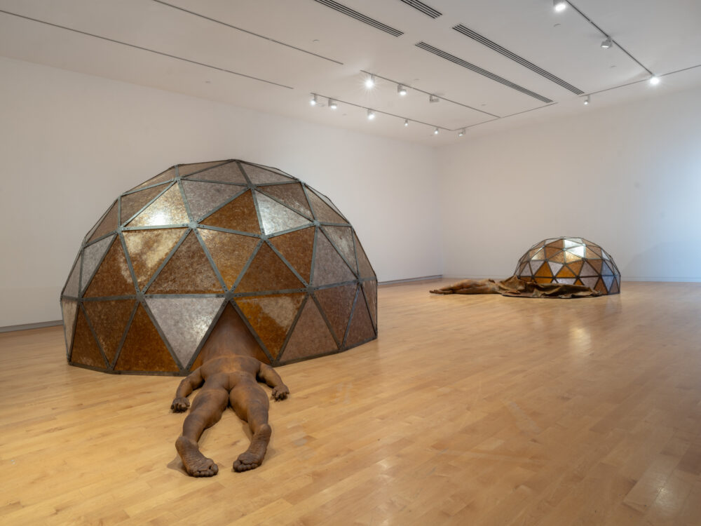 Two large-scale sculptures in a gallery with figures attached to geodesic domes.