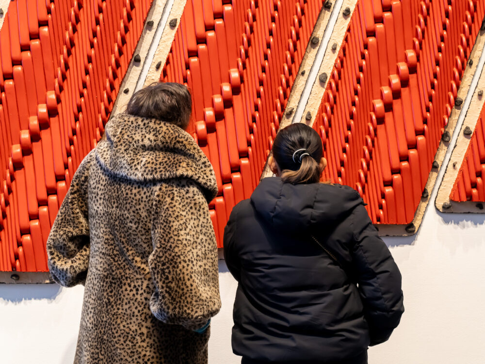 Two women looking at a red wall relief sculpture