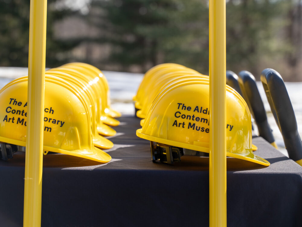 Yellow hard hats with The Aldrich's logo on a table.