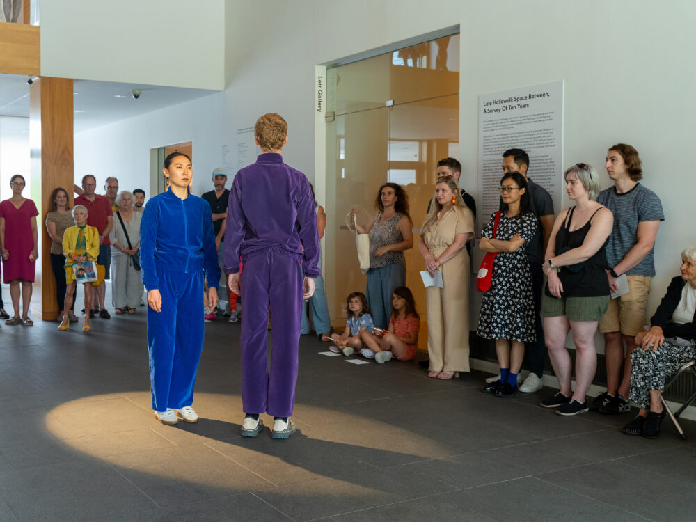Two dancers in blue and purple velour jumpsuits performing in an art gallery